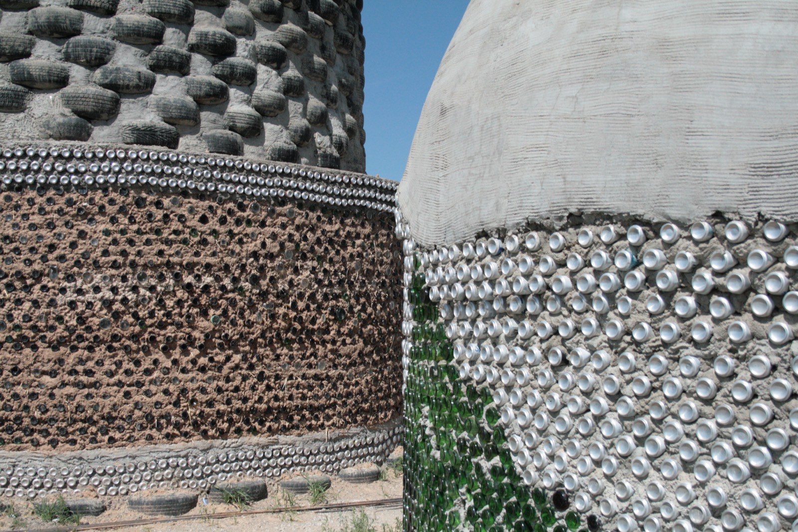 Exposed earthship walls showing rammed-tire courses above bottle-and-can infill walls rendered in adobe