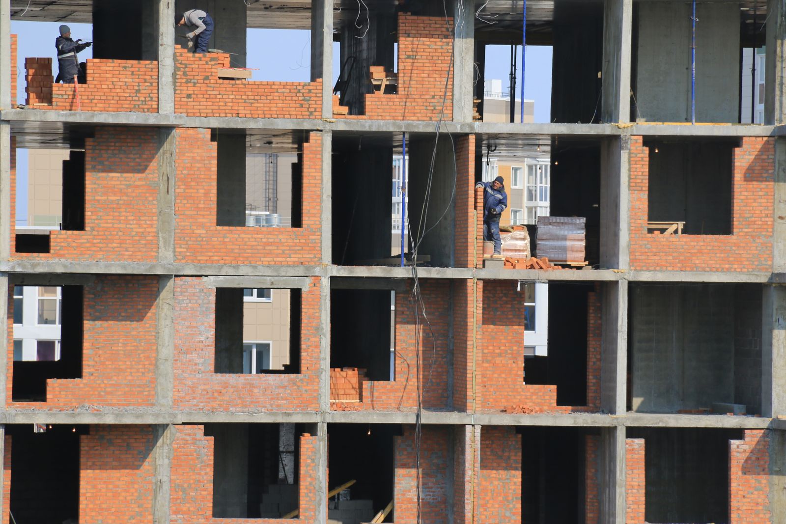 Construction workers laying brick by hand inside a finished concrete frame