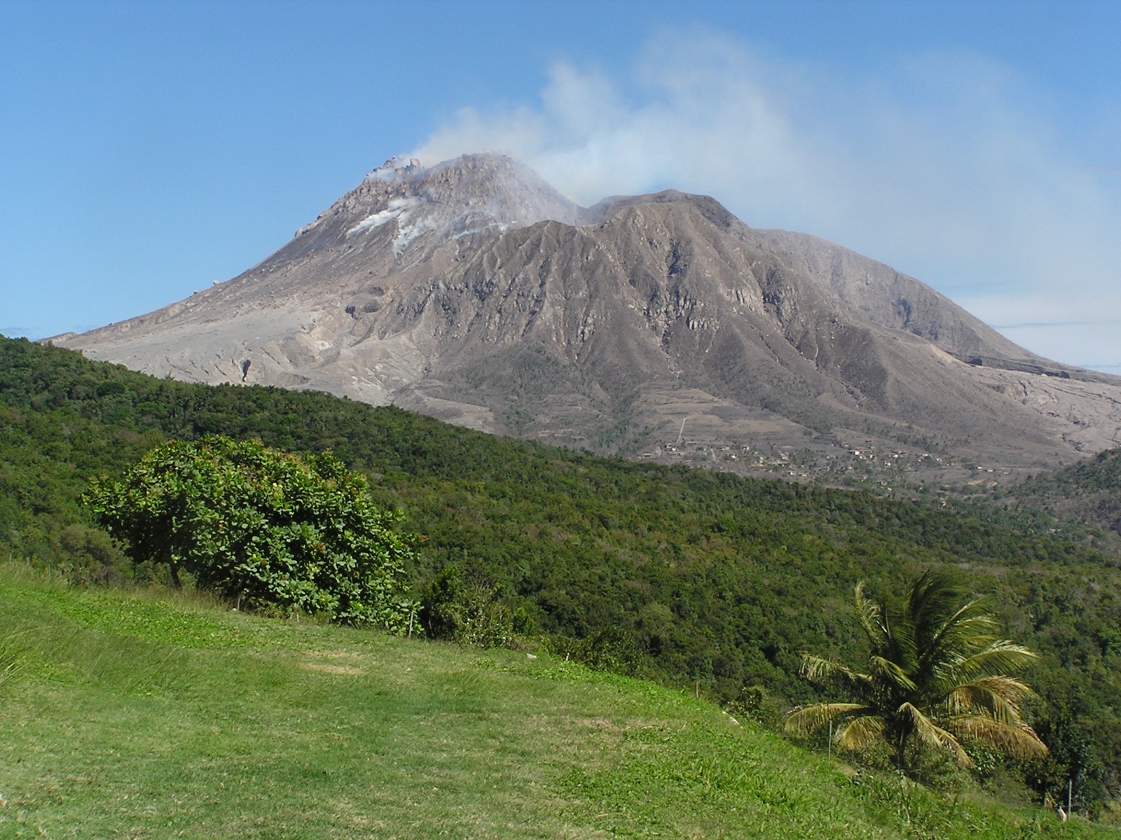 The steaming dome of the Soufriere Hills volcano on Montserrat, its grey ash-covered flanks rising behind green living hillside