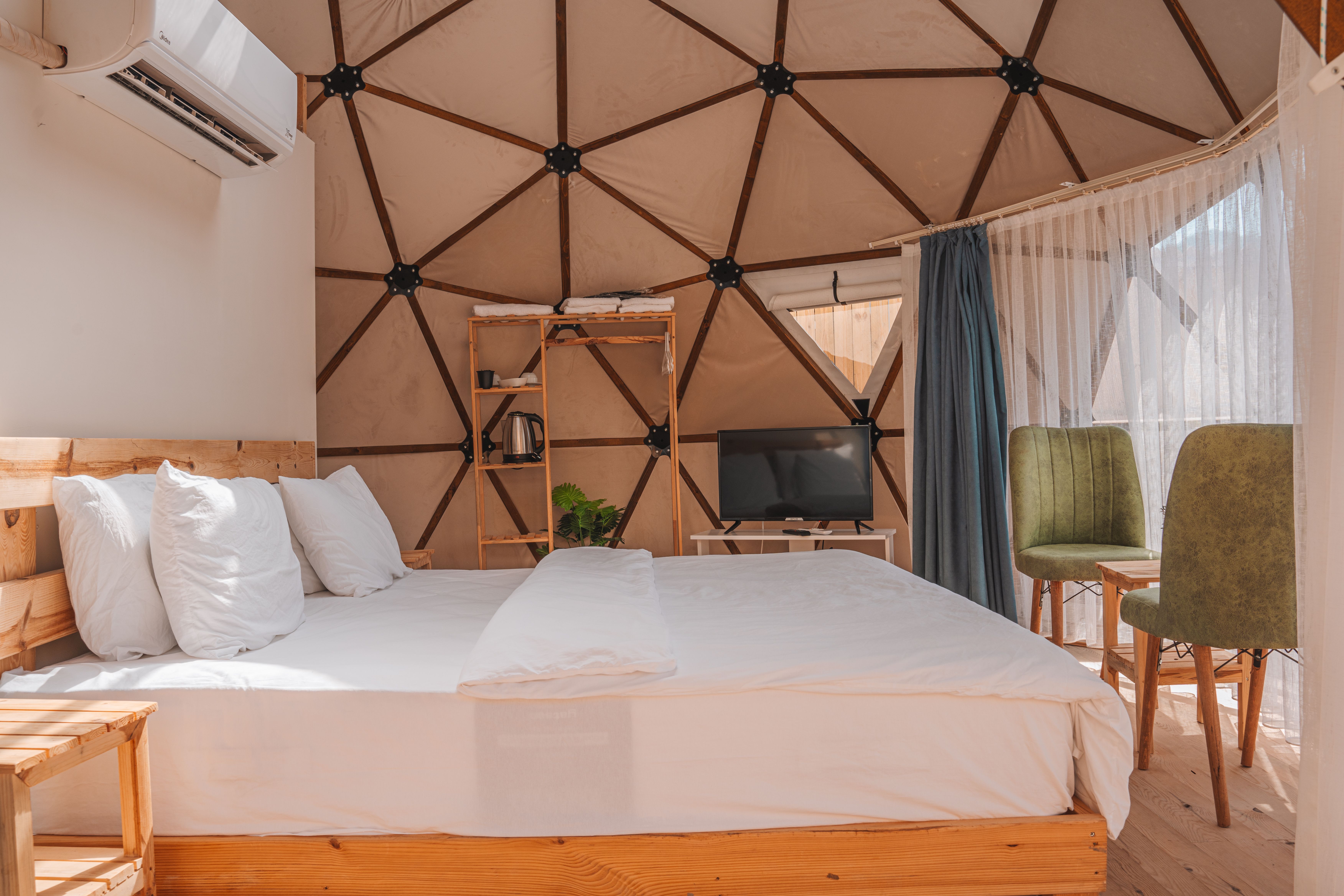 Interior of a geodesic dome showing the triangulated wood frame and black hub connectors, furnished as a bright modern room