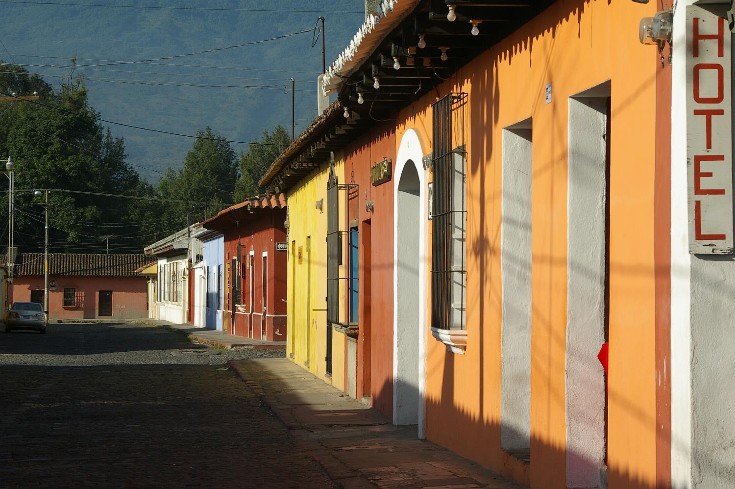 A cobblestone street of colorful colonial houses in Antigua, Guatemala, with a volcano rising behind